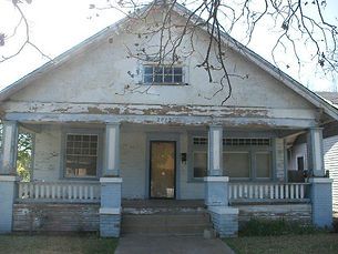 A weathered, light blue house with a porch and steps, under a partly cloudy sky.