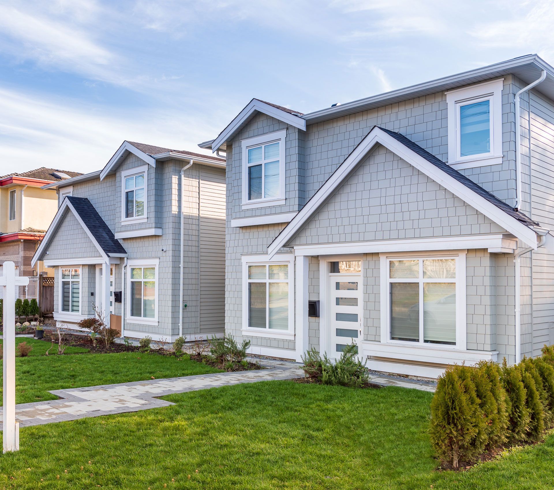 Two-story gray houses with white trim, green lawns, and blue sky.