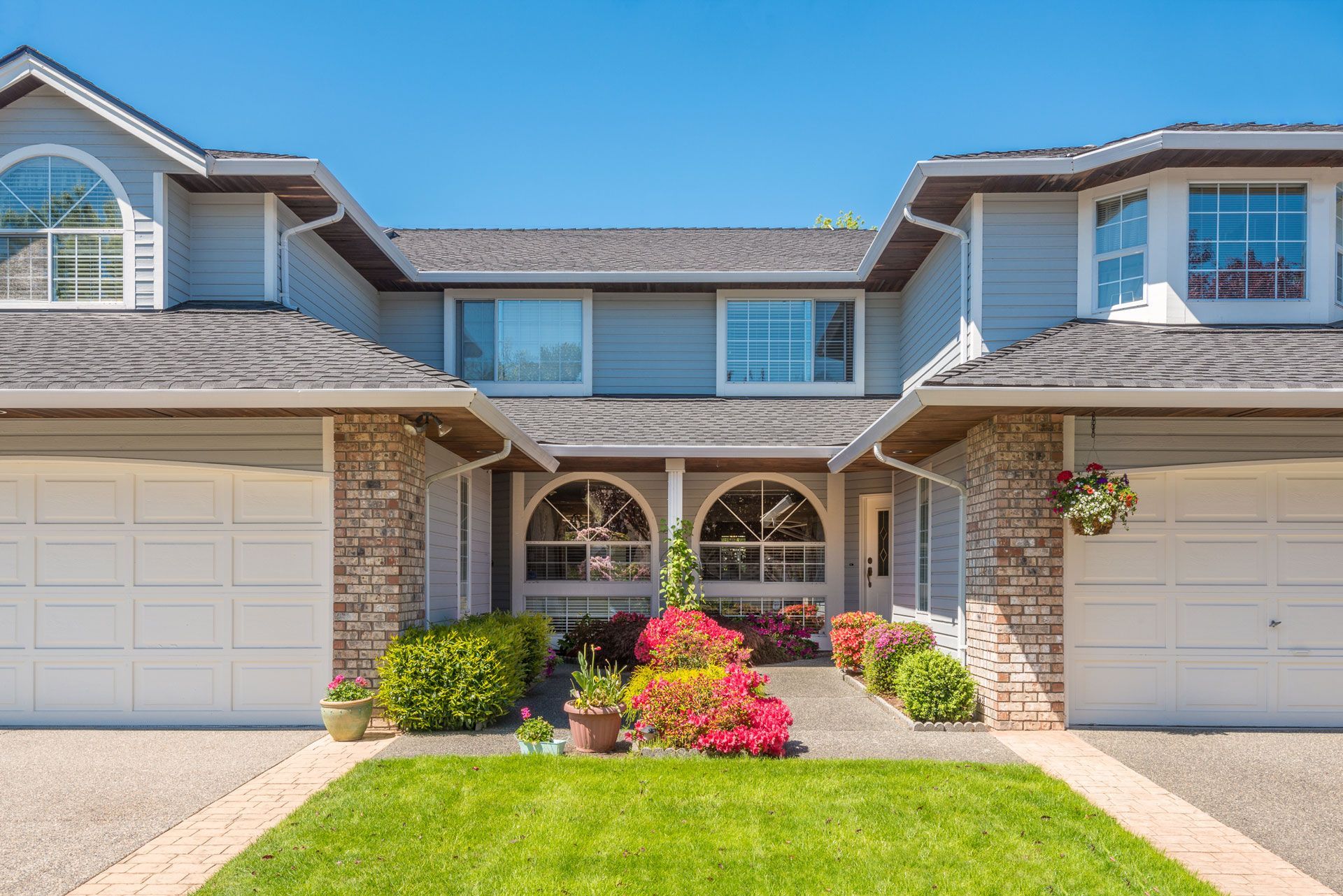 Gray multi-unit residential building with white garage doors and colorful flowers.