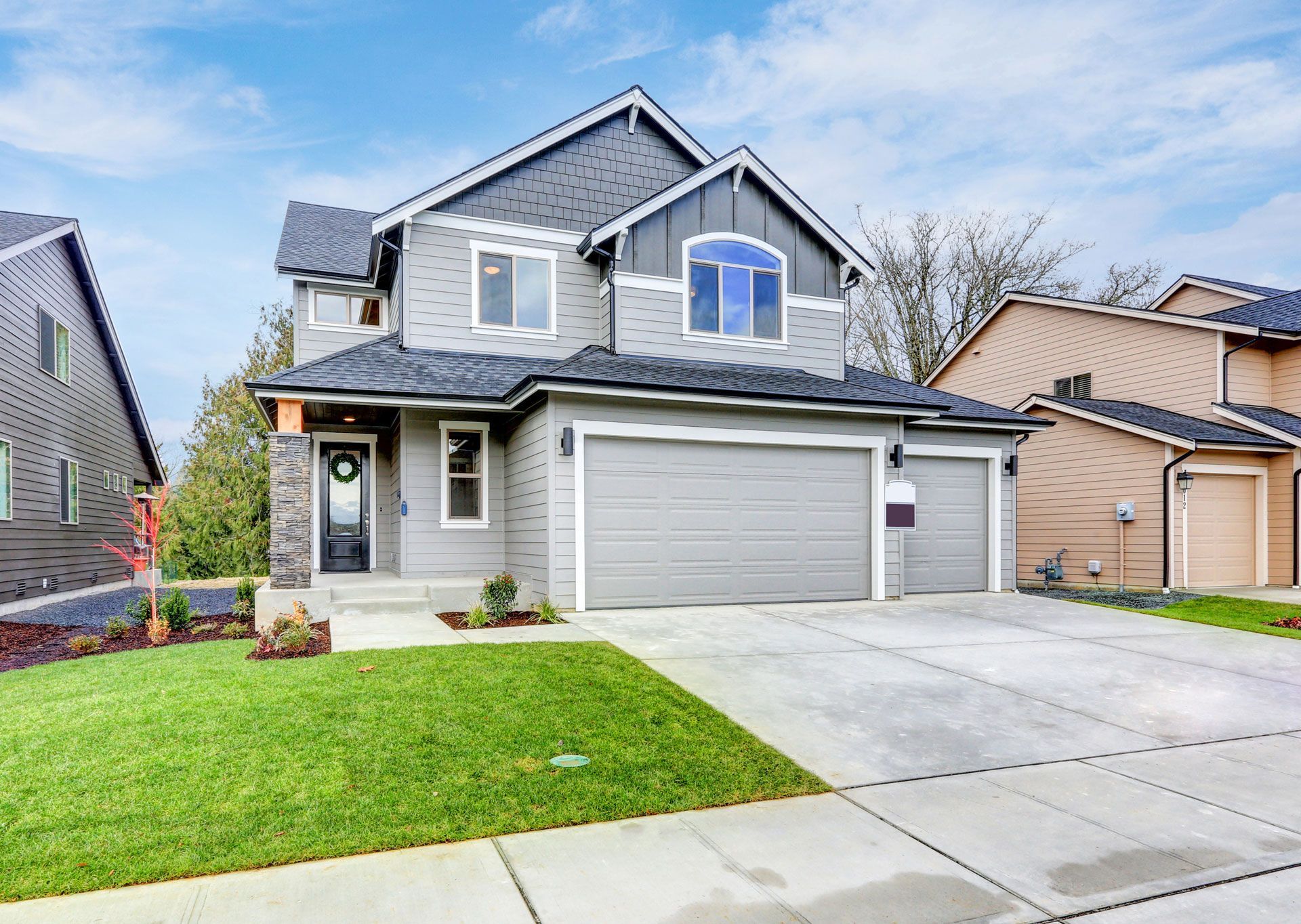 Two-story gray house with a three-car garage, green lawn, and blue sky.