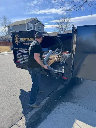 A man is loading a dumpster on a trailer.