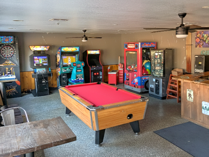 Game room with a red-felt pool table, arcade games, and a bar area.