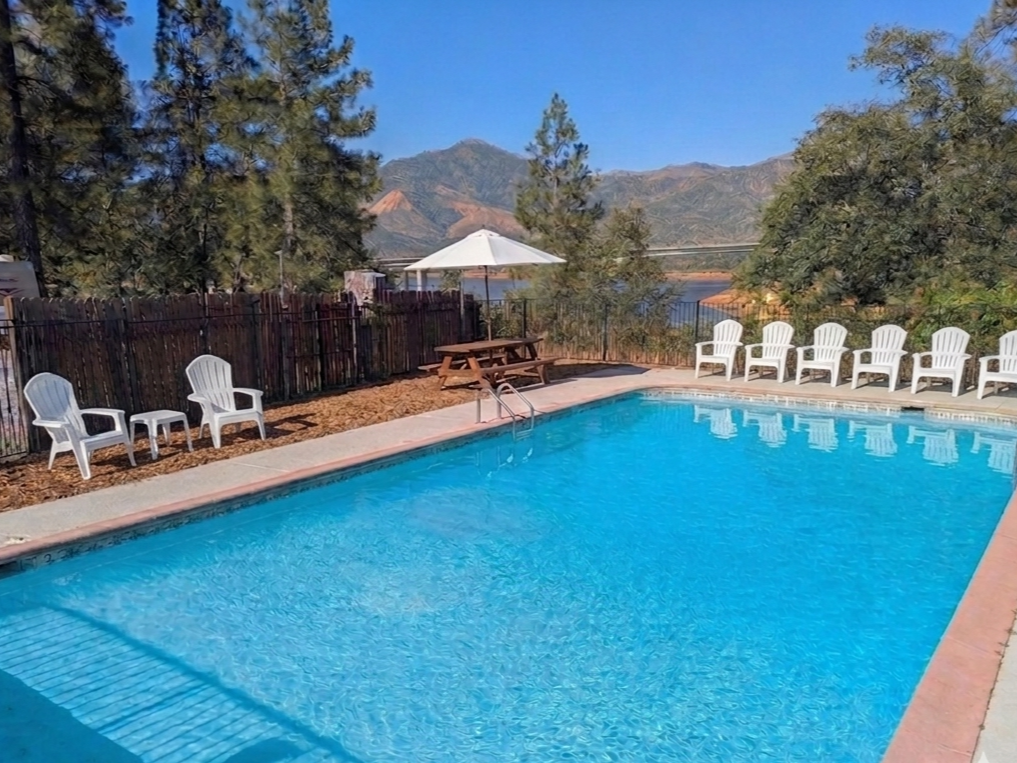 Swimming pool with blue water next to lounge chairs and a wooden building, a black fence, and a truck.