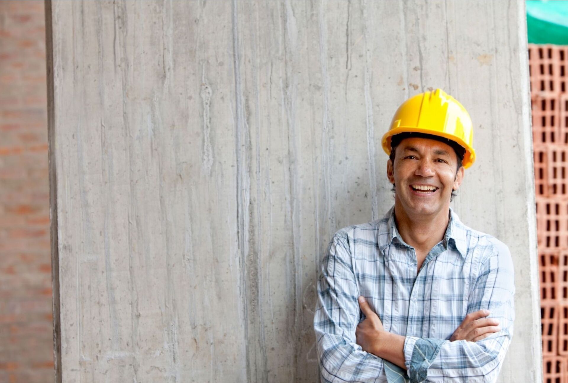 A construction worker wearing a hard hat is standing with his arms crossed and smiling.