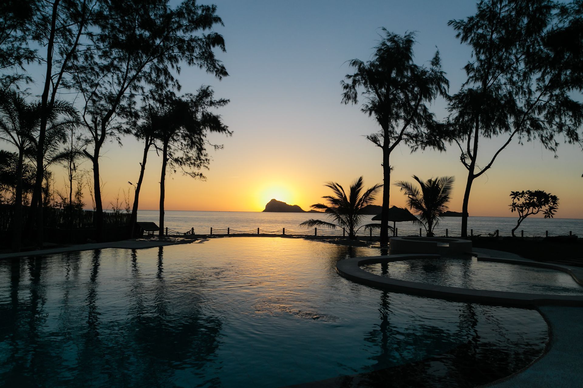 A sunset over a swimming pool with palm trees in the foreground
