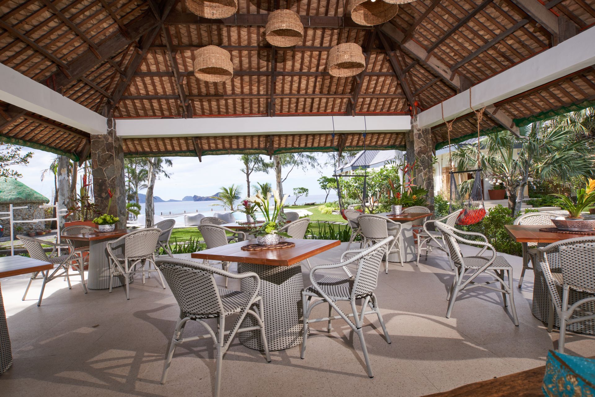 A restaurant with tables and chairs under a thatched roof.
