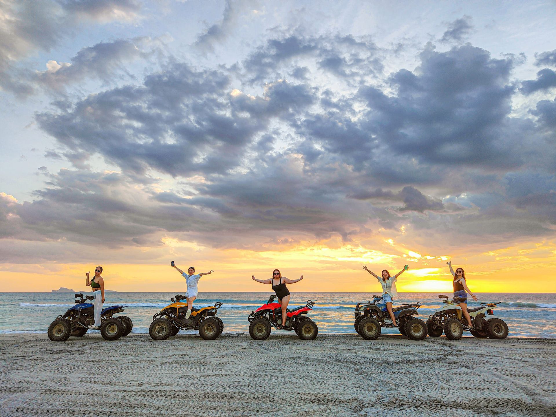 A group of people are riding atvs on the beach at sunset.