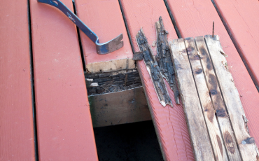 A photo of a deck that is in the process of being repaired due to rot. There is one deck board that has been ripped up and you can easily see that not only the board but also the frame underneath is slowly rotting away. 