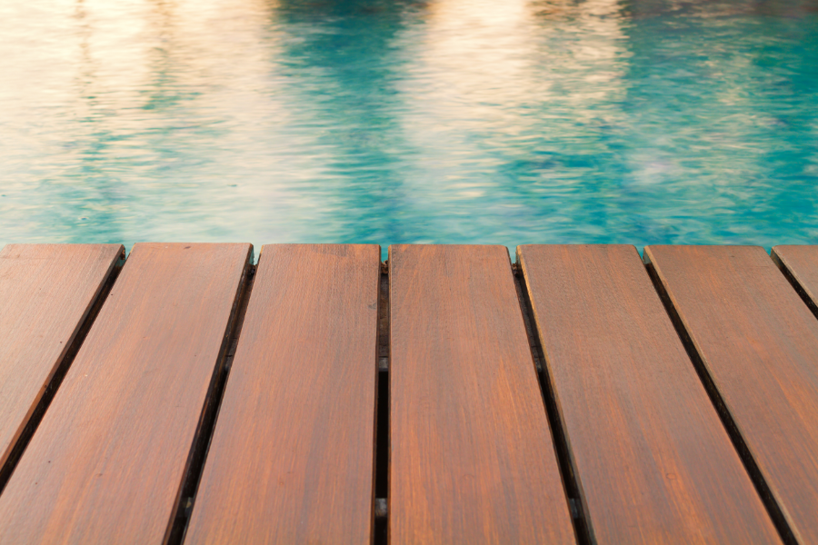 An up-close photo of the running boards of a pool deck that lead up to the edge of the pool. The deck is dark brown, and the pool is clean and refreshing.
