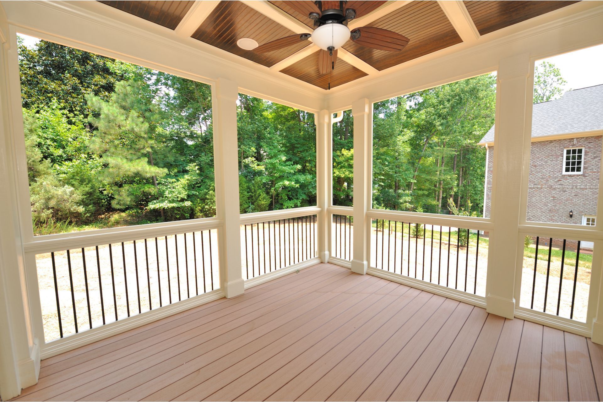 Screened porch with wood floor, fan, and forest view.