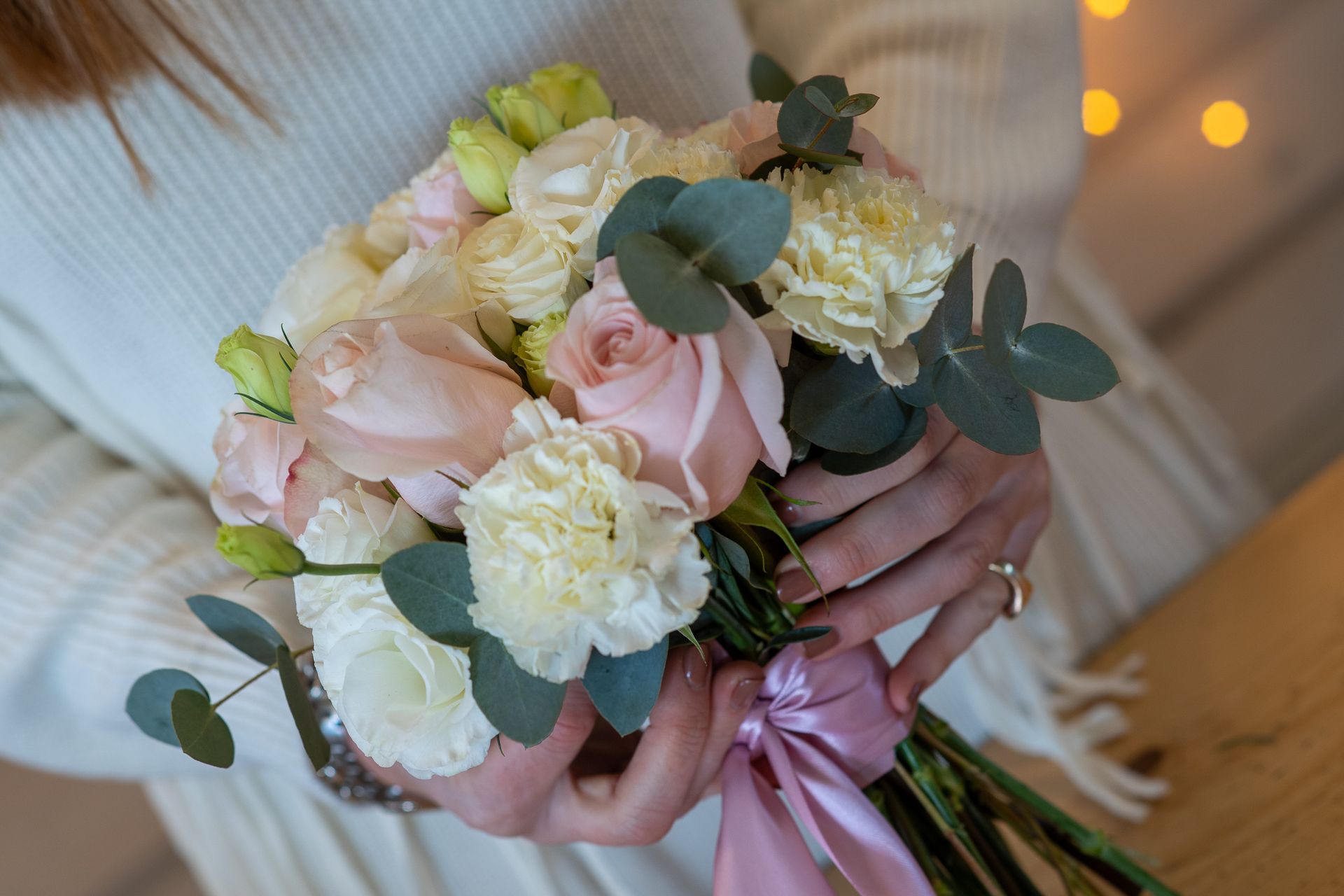 Mani che tengono un mazzo di fiori rosa e bianchi legati con un nastro rosa.