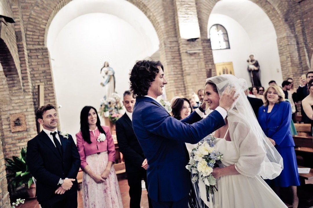 Lo sposo sistema il velo della sposa durante la cerimonia nuziale in chiesa. Gli ospiti guardano, illuminati dagli archi.