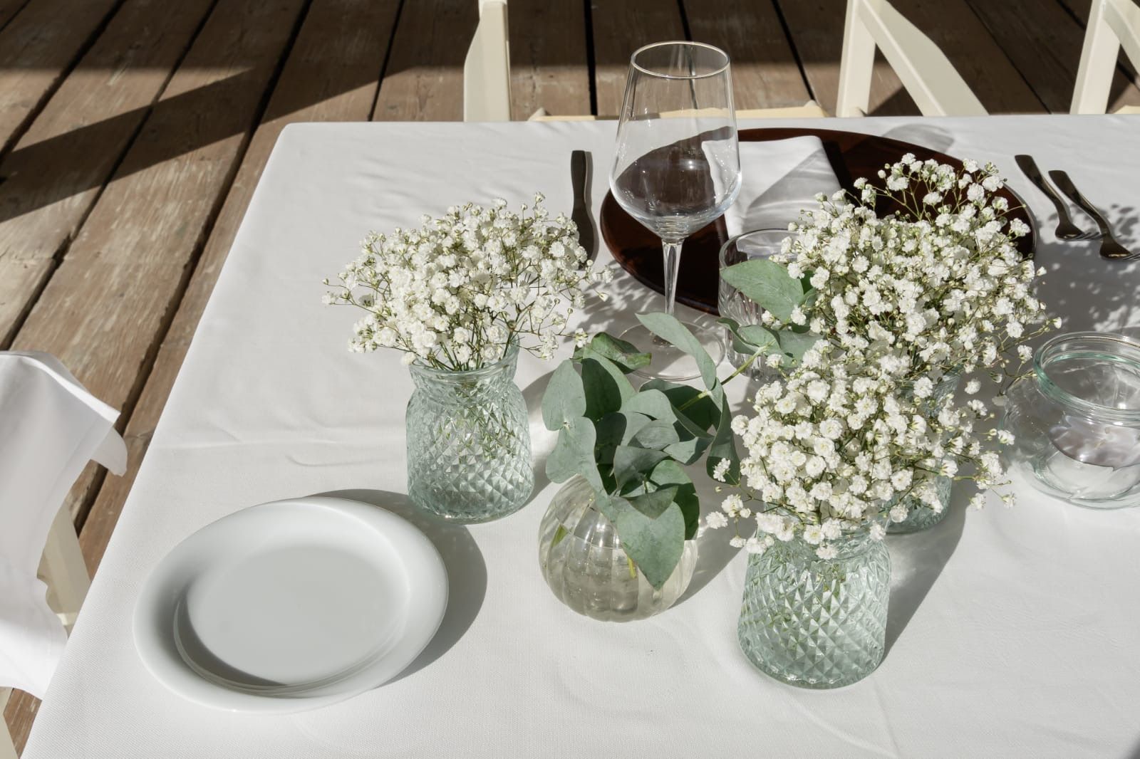 Apparecchiatura della tavola con fiori bianchi in vasi di vetro, piatti, posate e bicchieri per l'acqua su una tovaglia bianca.