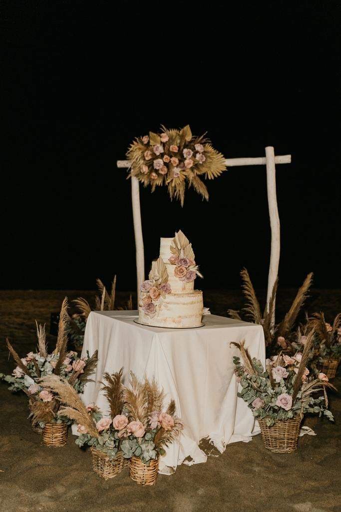 Torta nuziale su un tavolo, decorata con fiori, sotto un arco di legno, di notte.