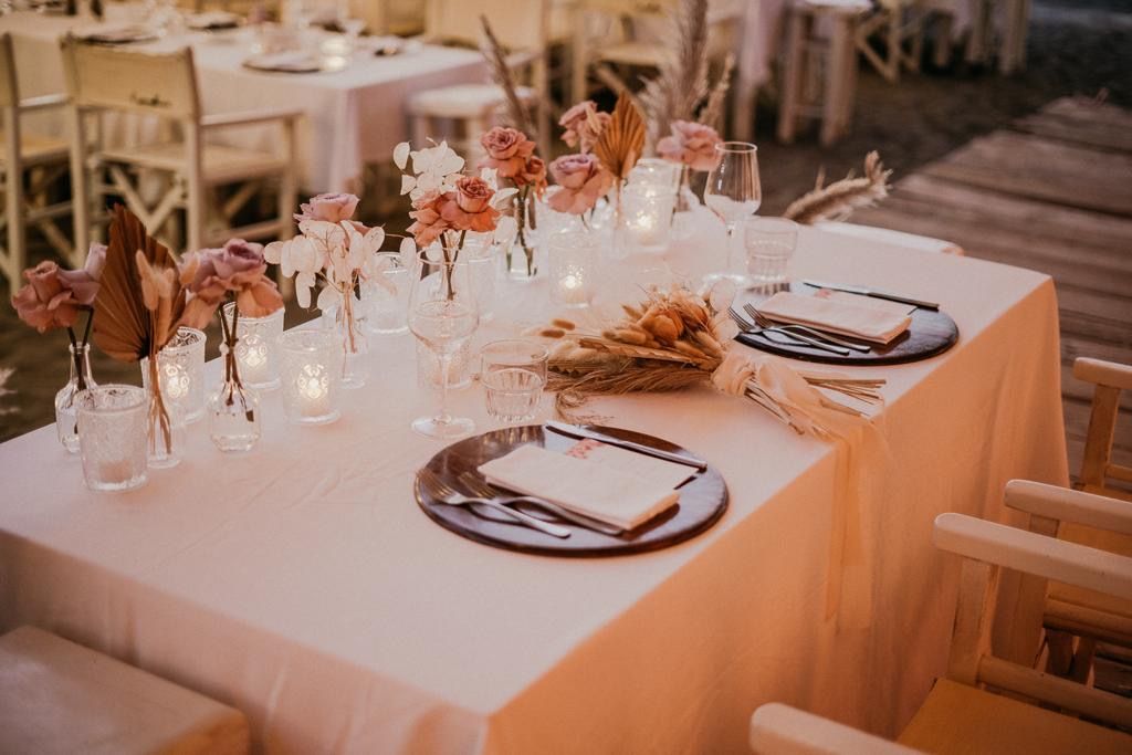 Tavolo del ricevimento nuziale apparecchiato con fiori, candele e posate. Luci soffuse.