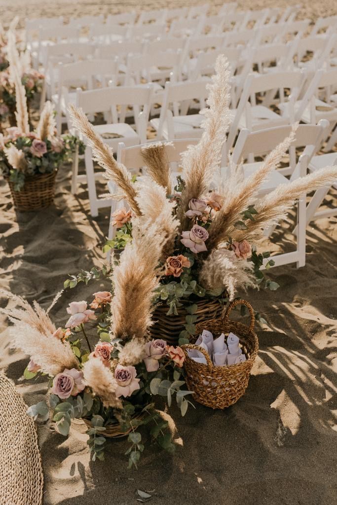 Cerimonia nuziale allestita sulla sabbia con composizioni floreali e sedie bianche.