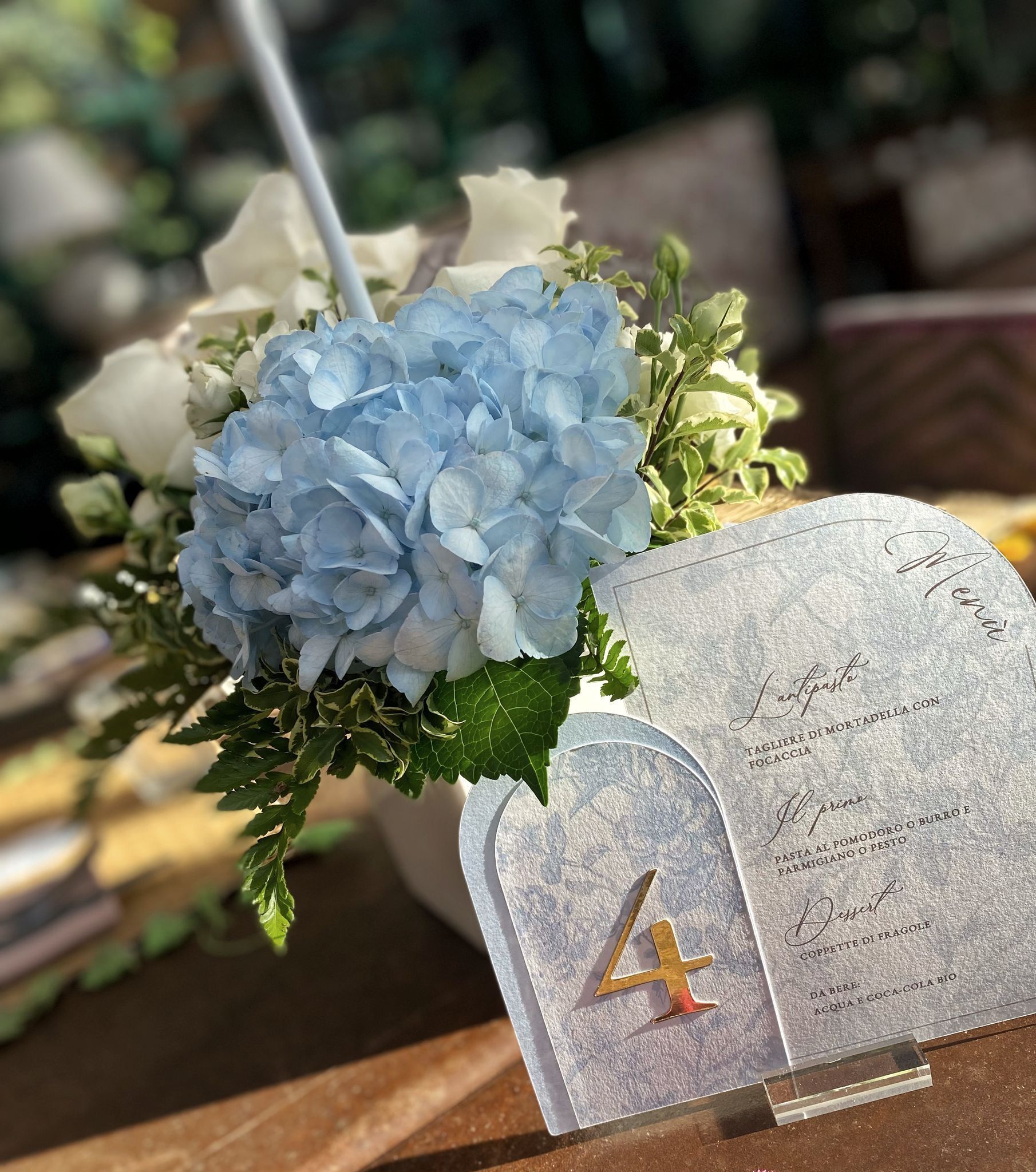 Composizione floreale con ortensie blu e rose bianche, accanto al tavolo numero 4.
