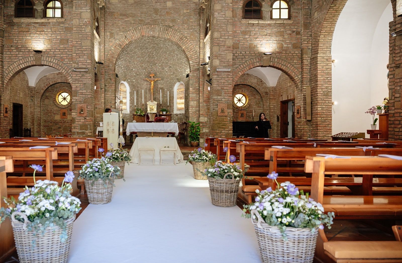 Interno di una chiesa addobbata per un matrimonio; navata con cesti floreali, panche, altare con croce.