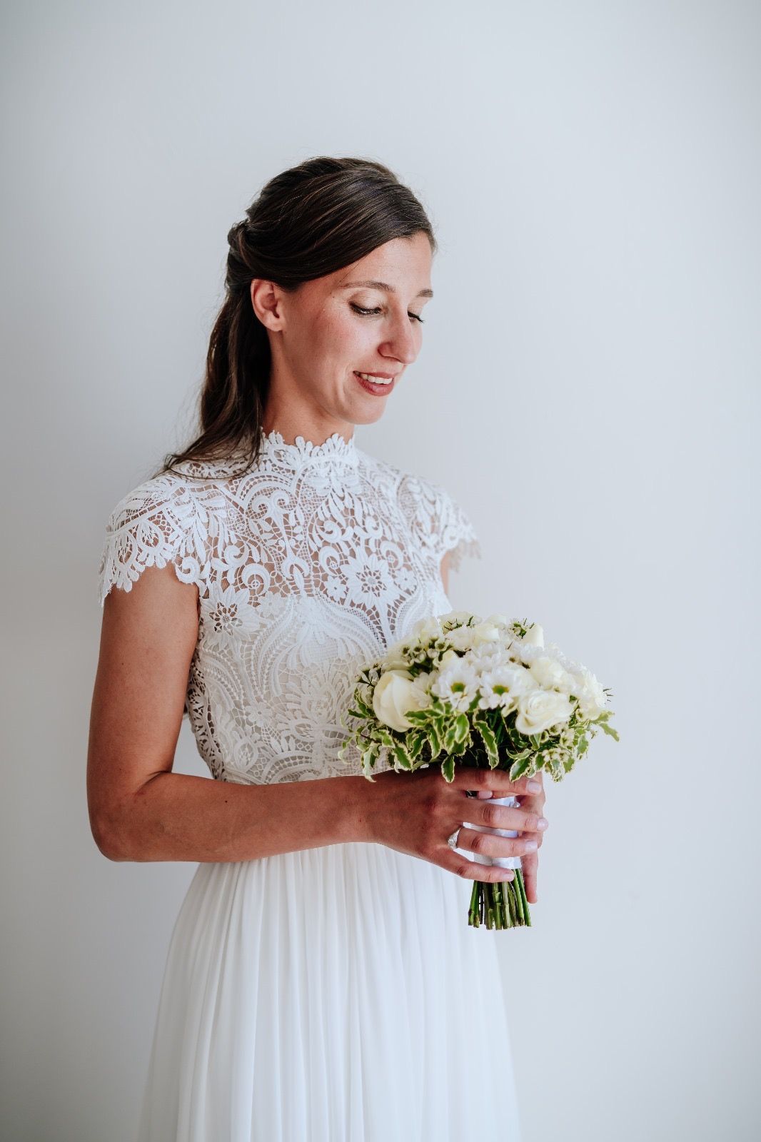 Sposa in abito di pizzo bianco che tiene in mano un bouquet di fiori bianchi.