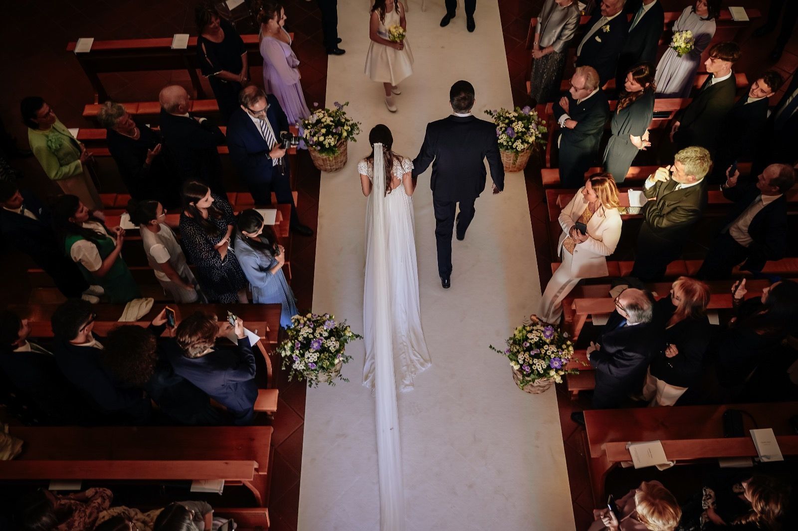 Gli sposi percorrono la navata. Tappeto bianco, composizioni floreali.
