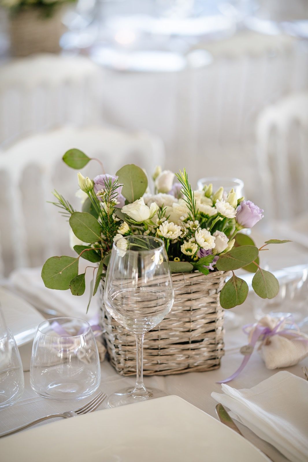Centrotavola floreale in un cestino di vimini su un tavolo apparecchiato per un matrimonio.