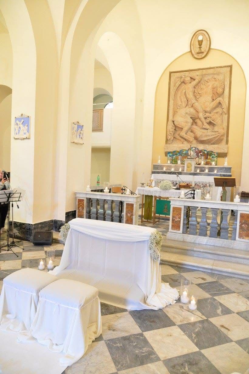 Interno di una chiesa addobbata per un matrimonio con posti a sedere drappeggiati e candele.