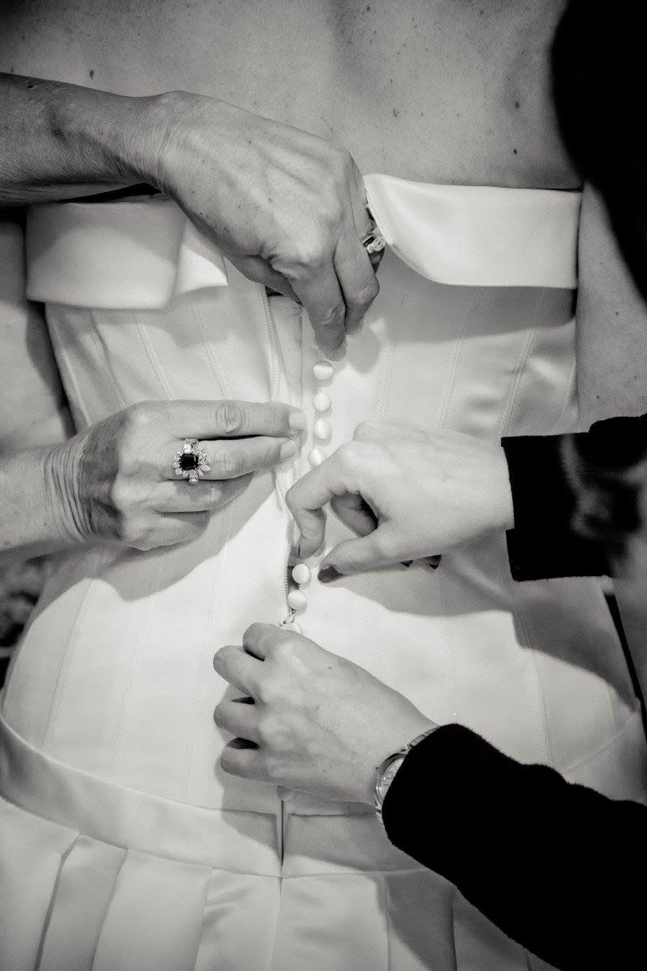 Due persone allacciano i bottoni sul retro di un abito da sposa bianco senza spalline.