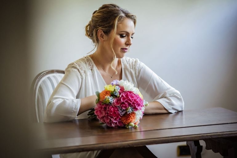 La sposa indossa un abito bianco e tiene in mano un bouquet, sorride mentre è seduta in macchina, con il velo.
