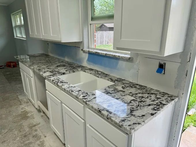 White kitchen cabinets and granite countertops with a double sink.