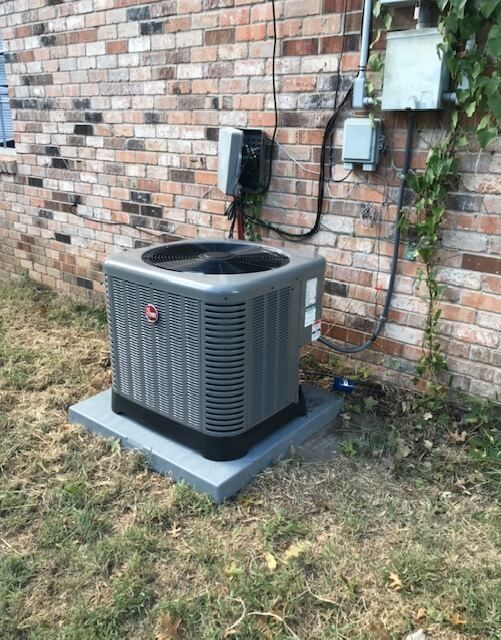 An air conditioner is sitting on the side of a brick building.