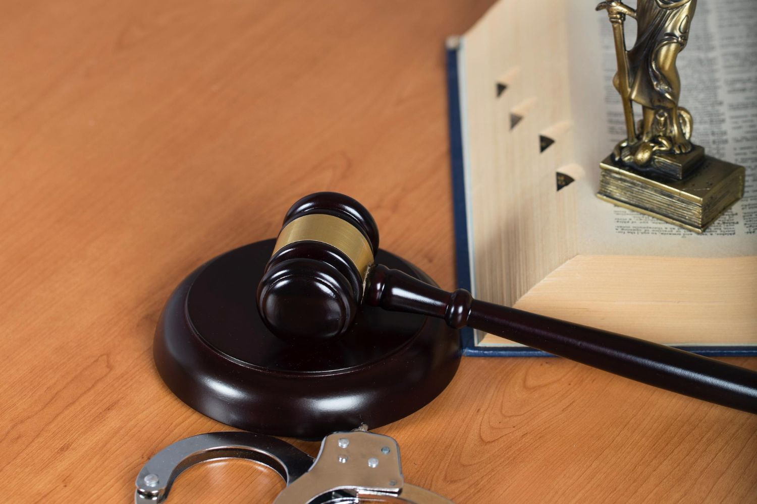 A judge 's gavel , handcuffs and a statue of justice are on a wooden table.