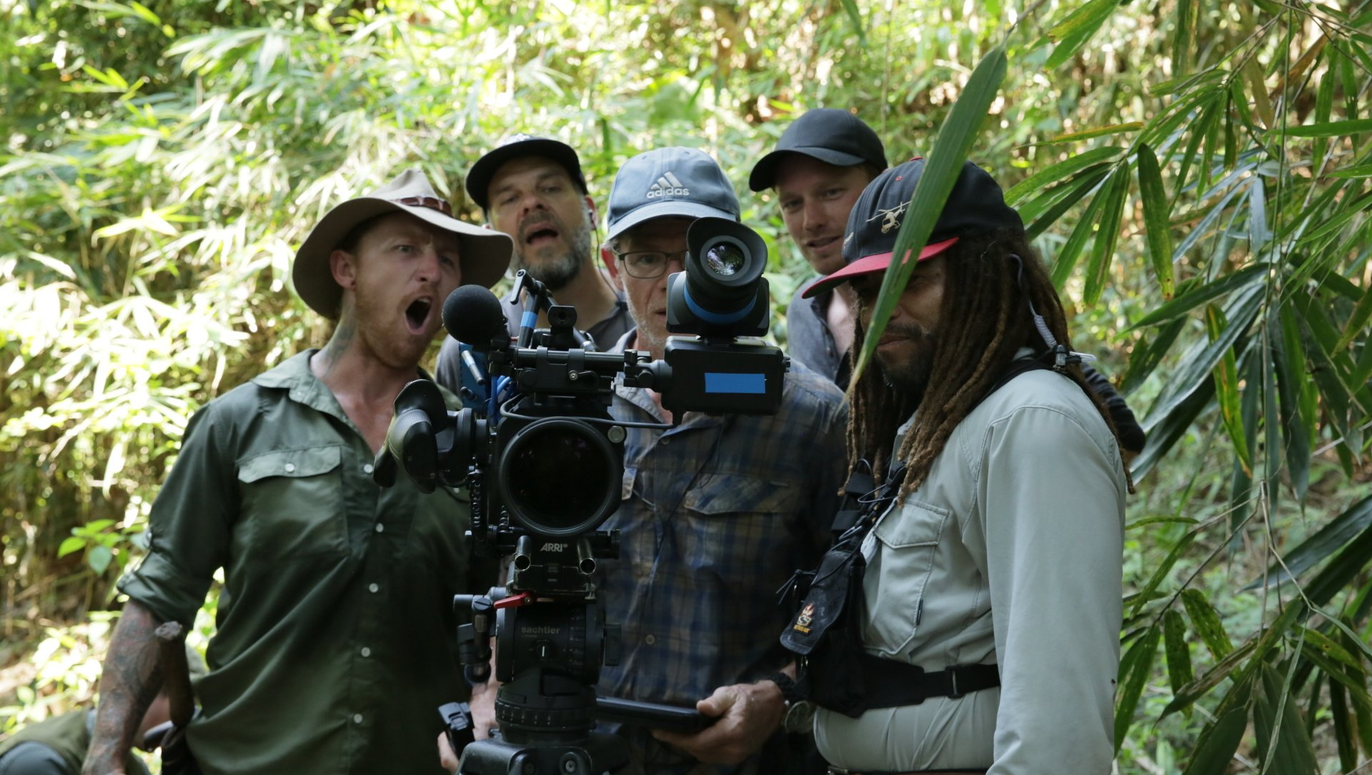 A group of men are standing in the woods holding cameras.