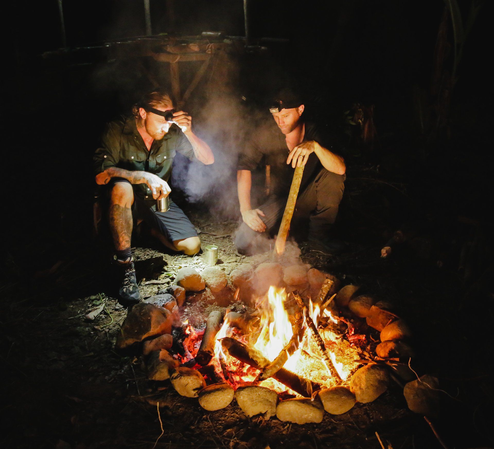 Two men are sitting around a campfire at night