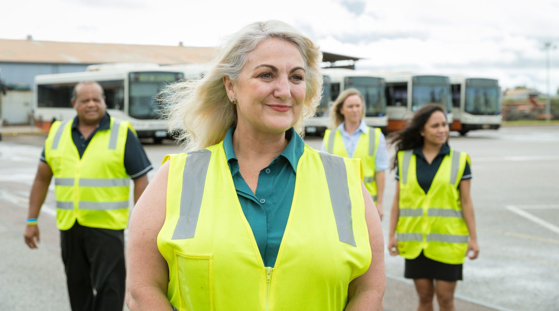 A group of people wearing yellow vests are walking down a street.
