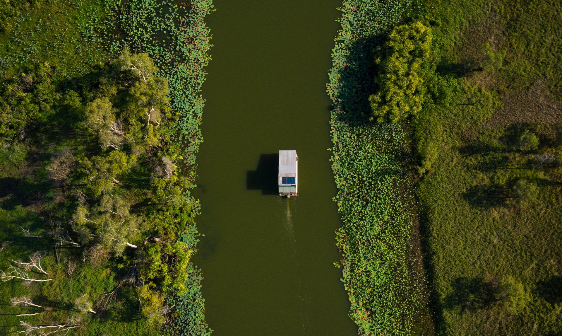 An aerial view of a truck driving down a river surrounded by trees.