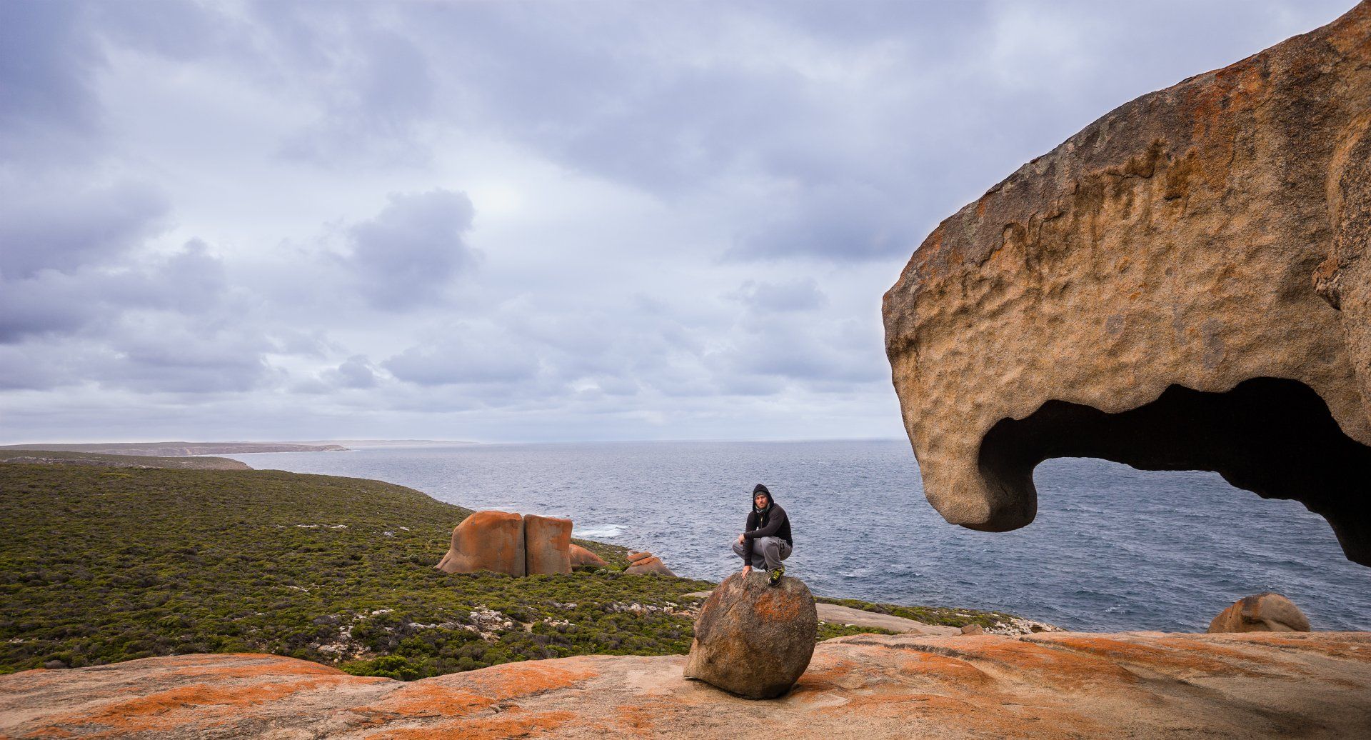 A man is sitting on a rock overlooking the ocean.