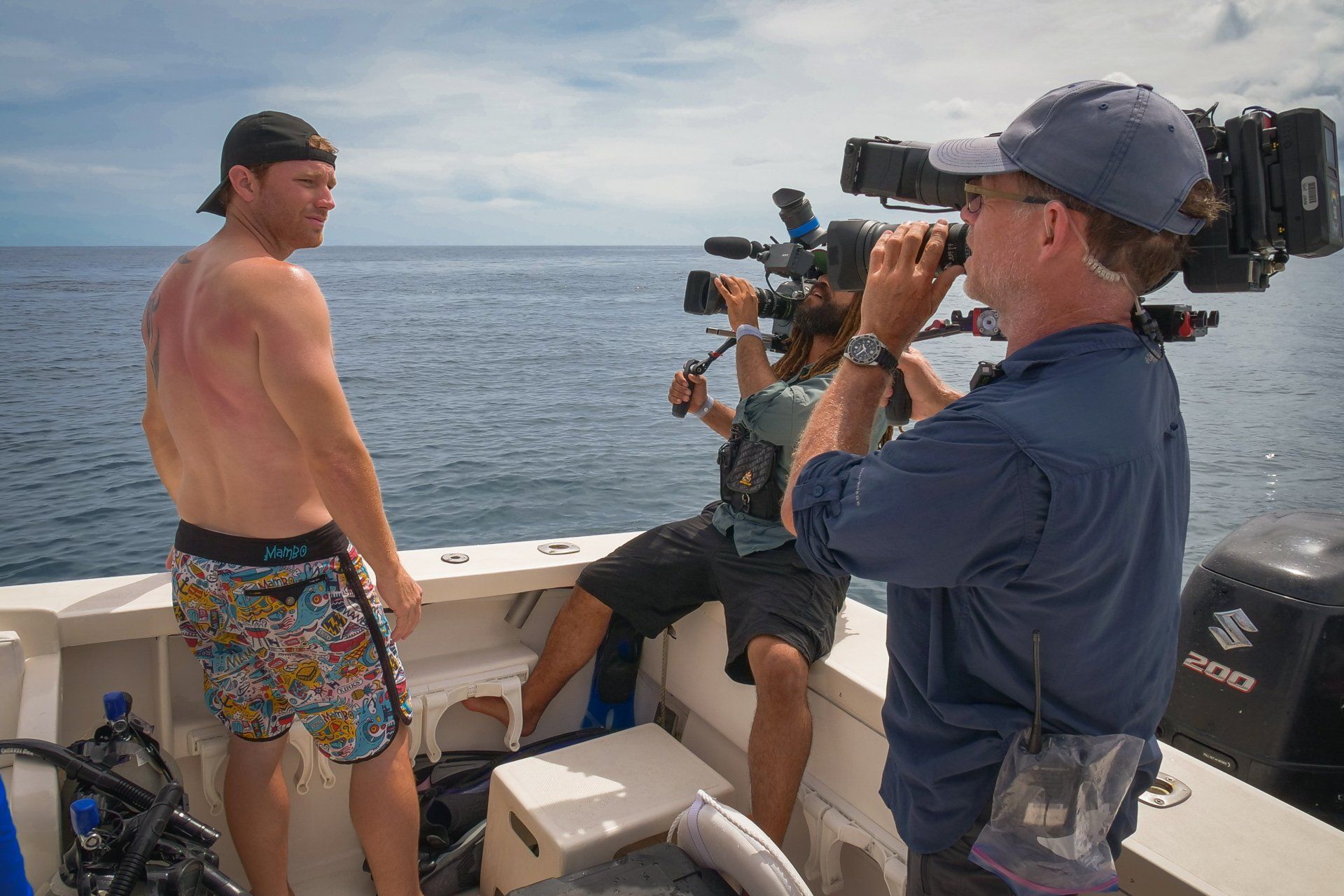 Two men are standing on a boat in the ocean while a man takes a picture with a camera.