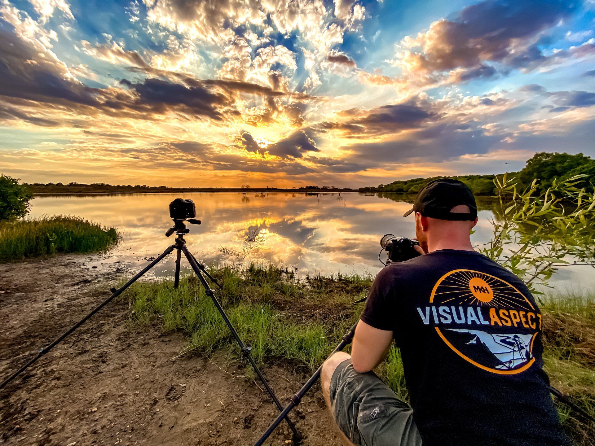 A man is taking a picture of a sunset over a lake.