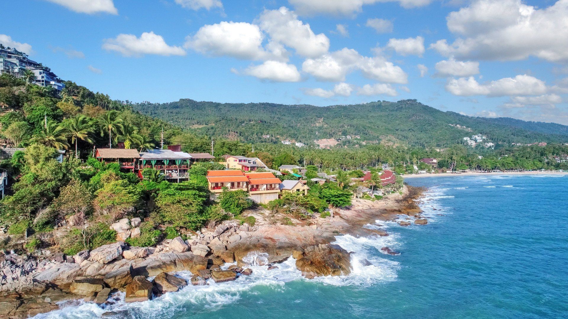 An aerial view of a cliff overlooking the ocean with mountains in the background.