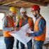 Construction workers in helmets and vests reviewing blueprints.