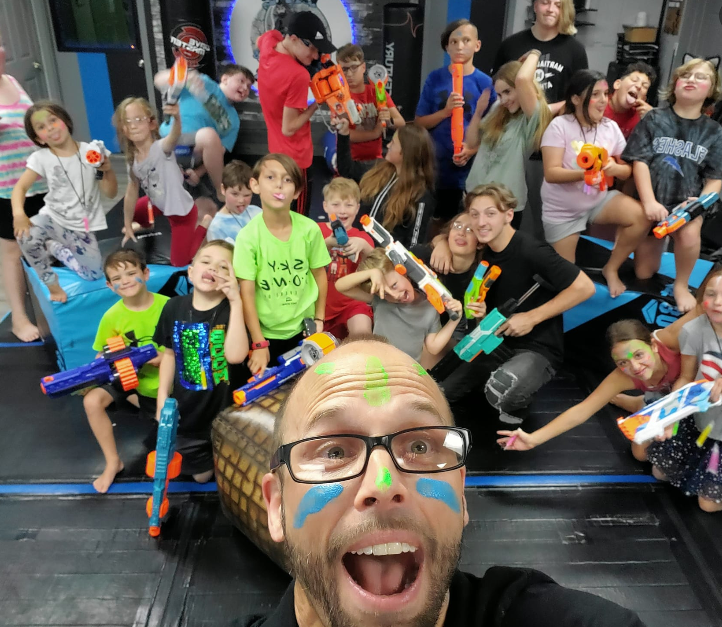 A man with glasses is taking a selfie with a group of children