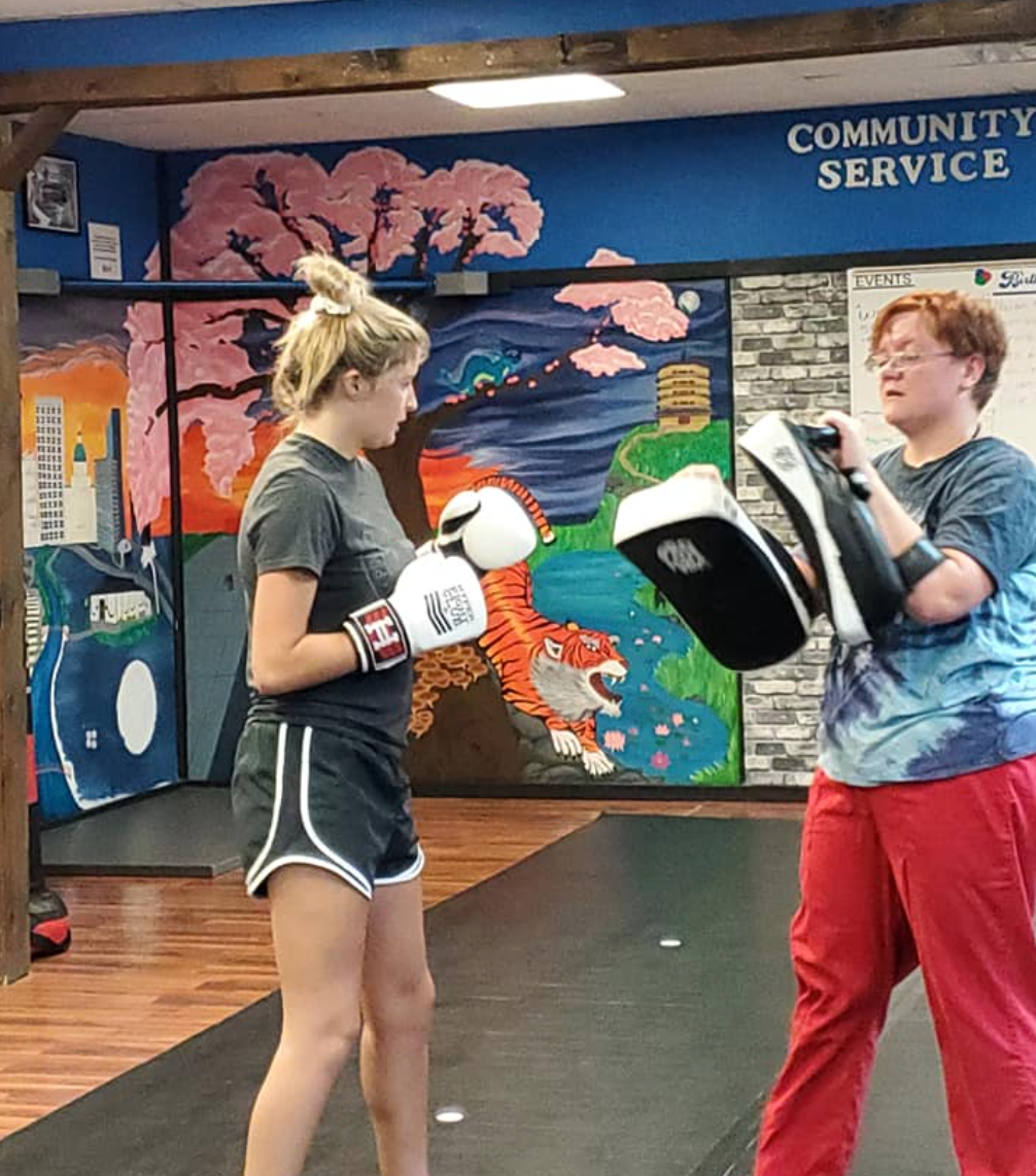 Two women are boxing in a gym with a sign that says community service