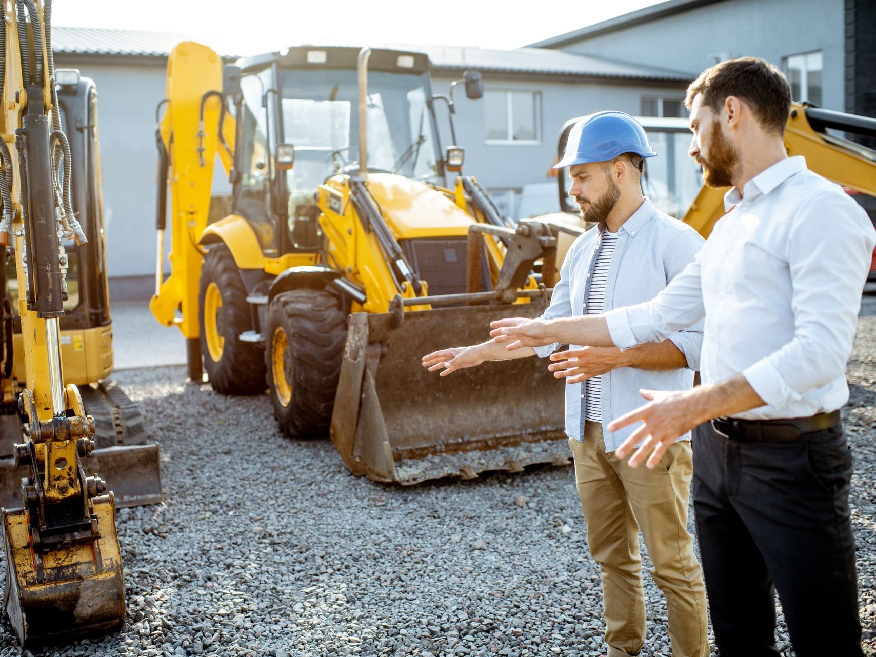 two men are standing next to each other in front of construction machinery .