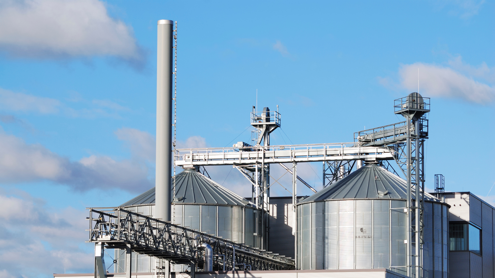Silos industriales plateados con tuberías y pasarelas contra un cielo azul.
