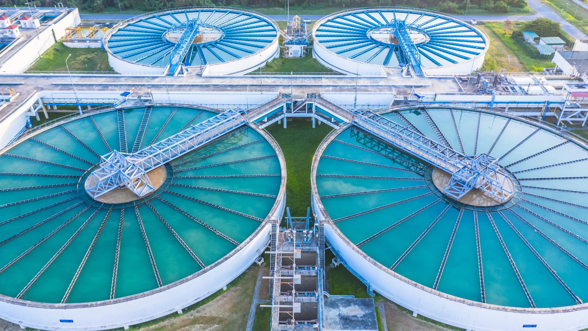 Vista aérea de una planta de tratamiento de aguas residuales con tanques circulares, agua turquesa y estructuras de concreto.