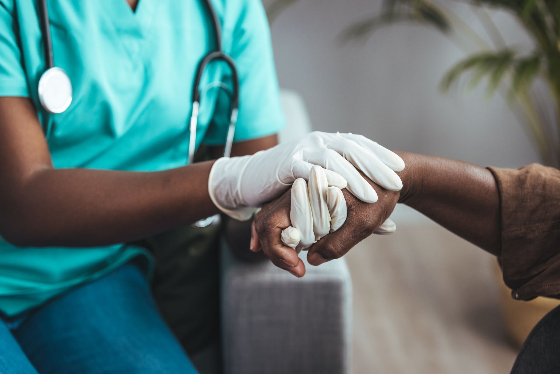 Medical professional in blue scrubs and gloves holds the hand of a patient, indoors.