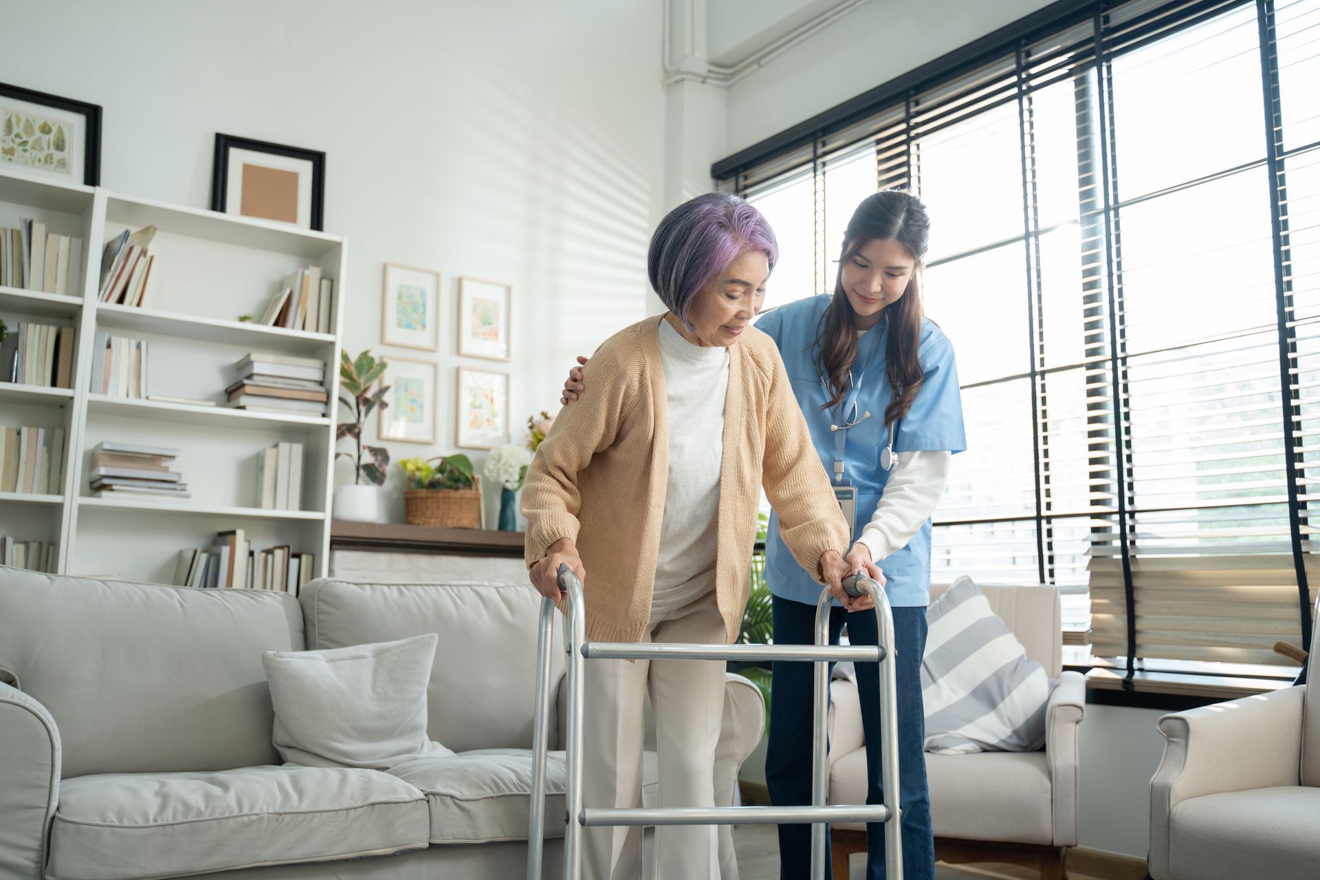 A caregiver assists a person using a walker in a living room.
