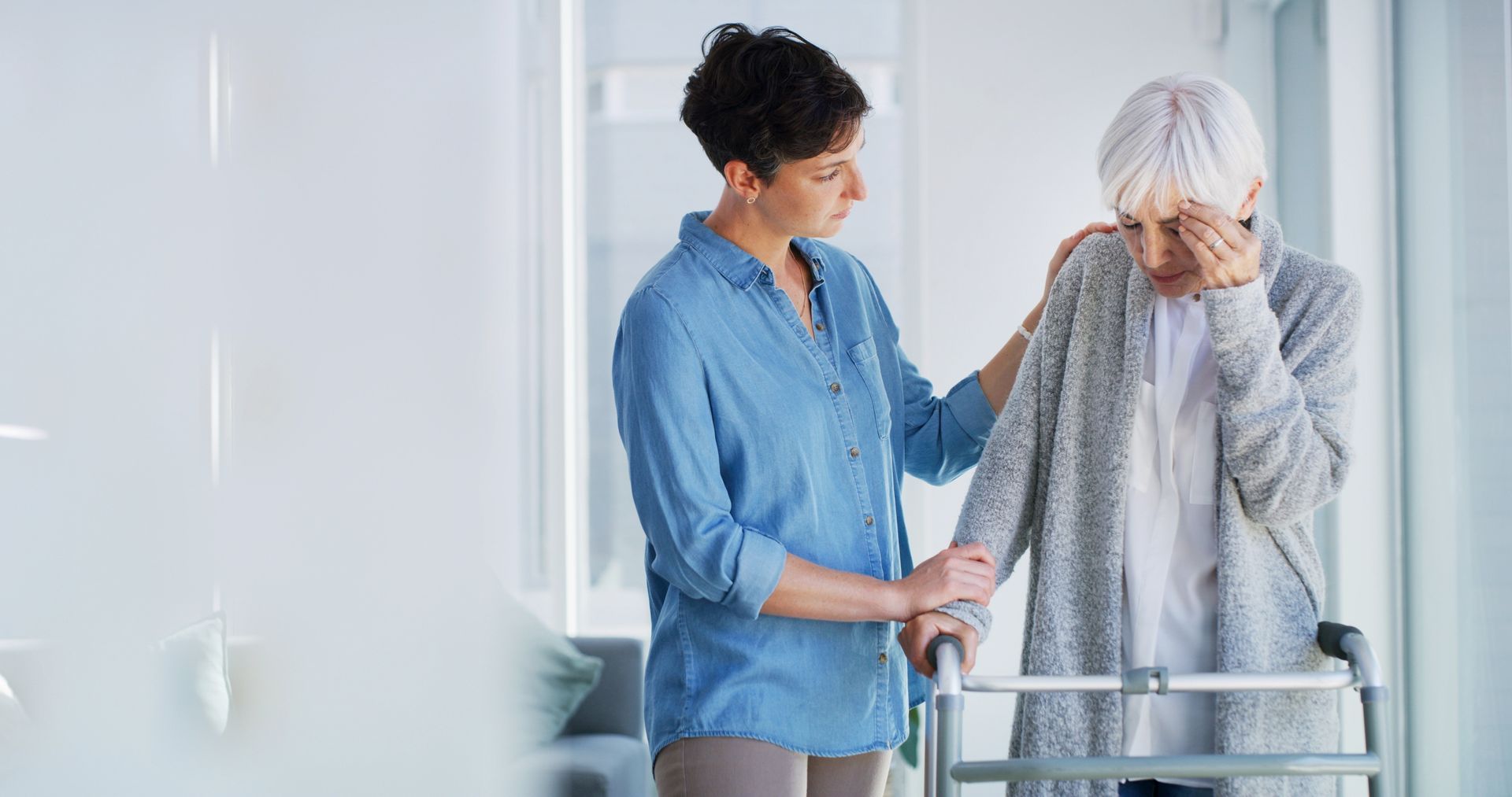 Woman comforting another woman who is using a walker; the older woman is crying.
