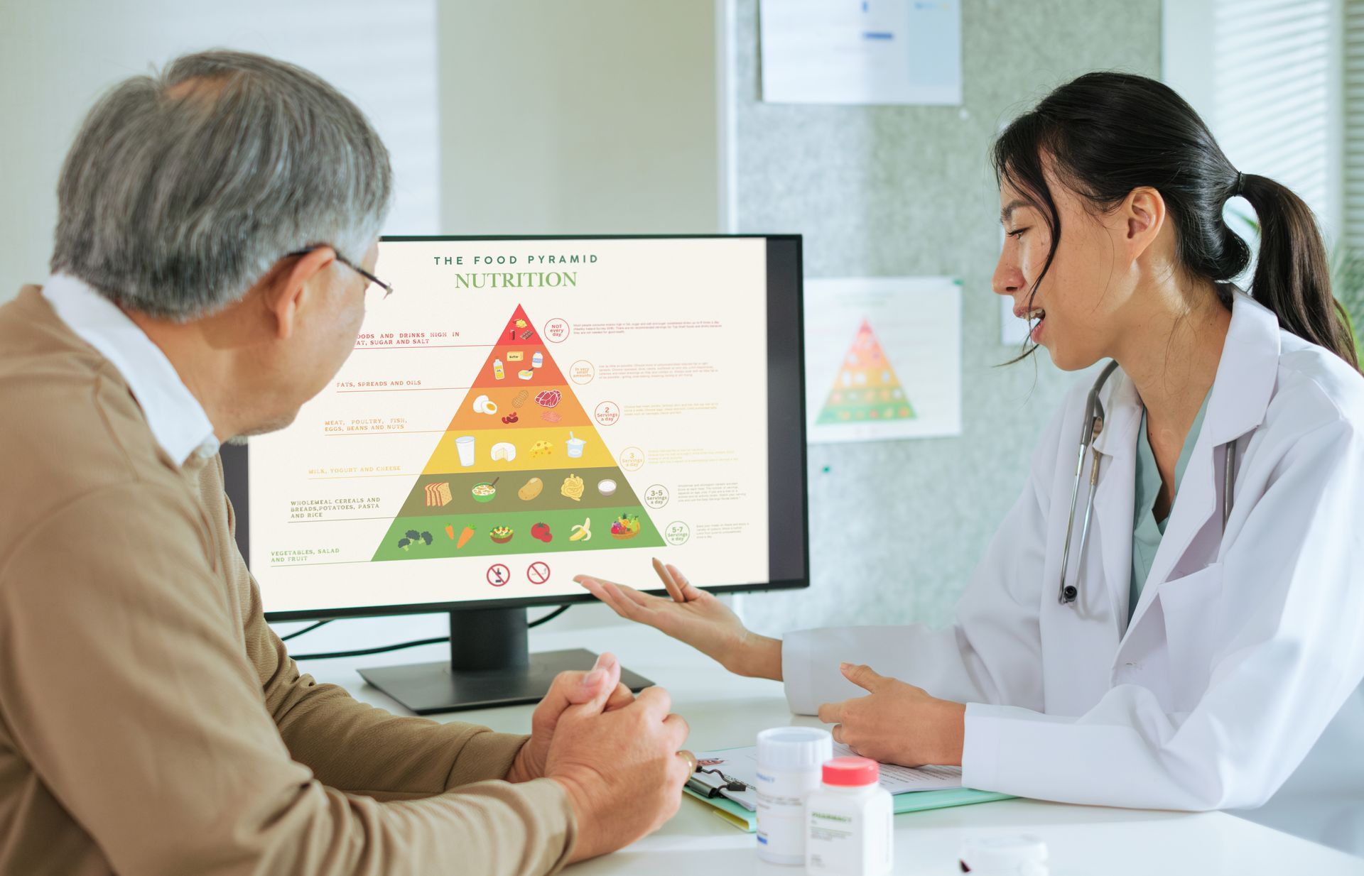 Doctor points to nutrition pyramid on screen, explaining it to a patient in an office.