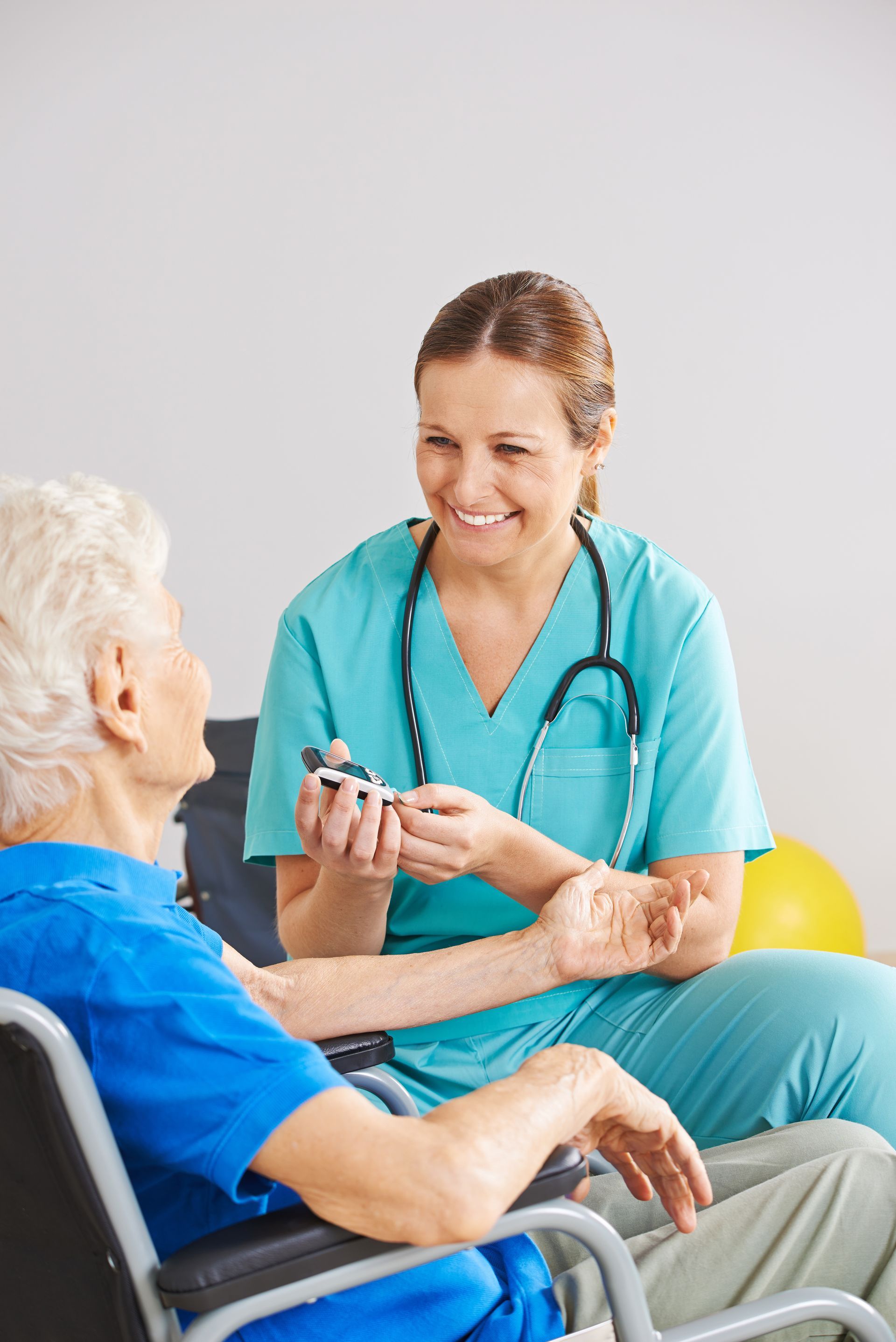 Nurse taking the blood sugar of an elderly person in a wheelchair; both smile.